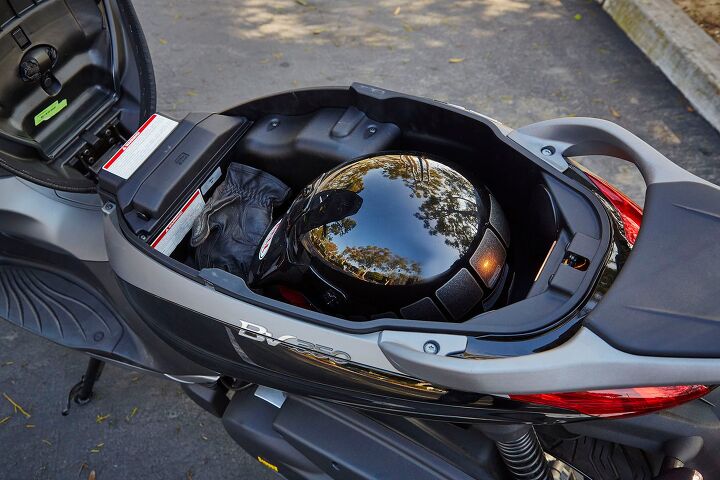 2015 piaggio bv350 i e review, A front hinging seat makes the storage compartment readily accessible There s only room for one helmet but note the little pouch underneath the seat itself above the green sticker That s a waterproof cover for the seat another nice detail that helps separate the BV350 from the rest