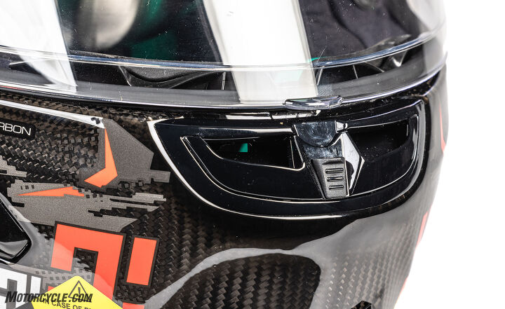 motorcycle com mega helmet shootout, You can see the carbon fiber weave throughout the X 803 lending to its light weight Also shown is the chin vent which is shaped in such a way as to guide the finger to the tab in the middle of the visor to pop it open Clever