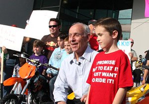 malcolm smith sells 3 banned vehicles, Malcolm Smith poses with a child The shirt reads I promise not eat it I just want to ride it