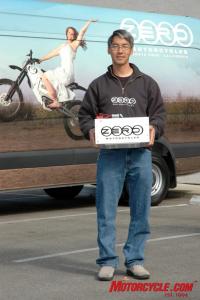 2008 zero x electric motorcycle review motorcycle com, Neal Saiki holds the heart of the Zero X electric motorcycle a revolutionary battery We know that Neal is the brains behind the bike and not the marketing guy cause if he were we doubt he would ve chosen the brand image you see behind him