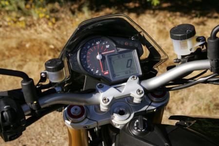 2011 aprilia dorsoduro 1200 review video motorcycle com, The tidy gauge cluster actually reveals a lot A large analog tach dominates but the digital display has a speedo clock odometer tripmeter just one engine temp ride mode and gear position indicator